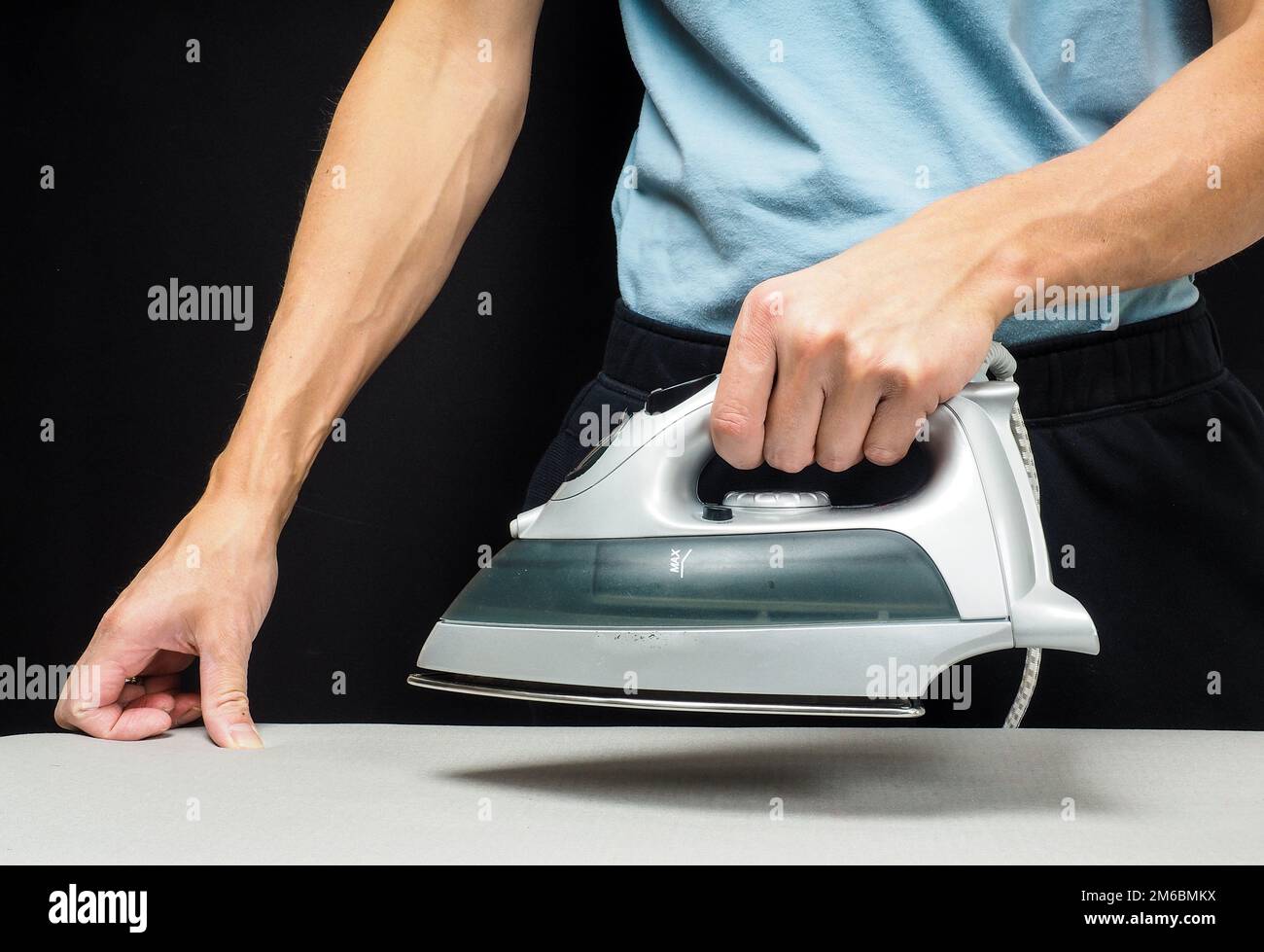 Male person using a steaming hot iron, on a iron board on black Stock Photo