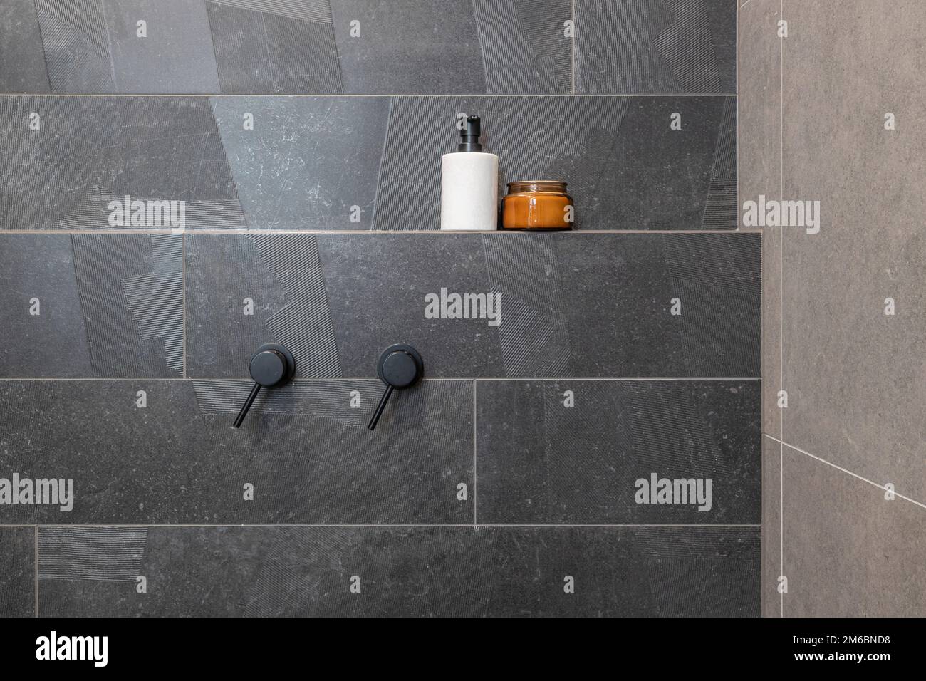 tiled bathroom shower area showing black hot and cold taps Stock Photo