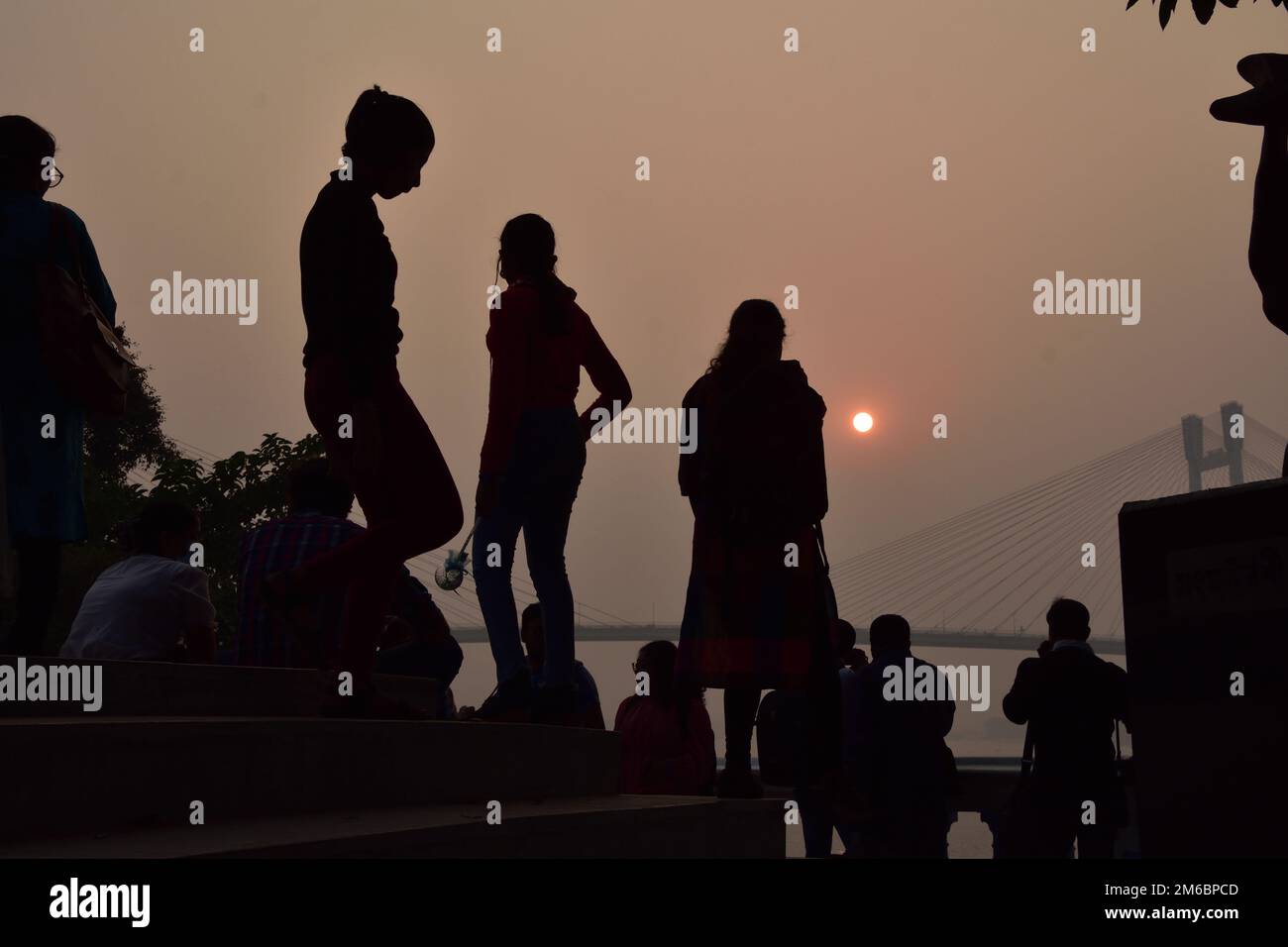 Non Exclusive: Dec 31, 2022, Kolkata, India. Persons enjoy  the sunset across the   Howrah Bridge (Vidyasagar Setu) On River Ganges. scenic beauty of Stock Photo