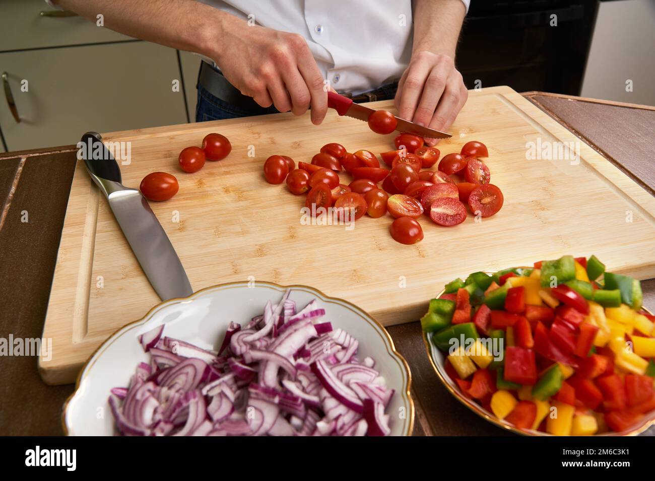 Man's hands cutting fresh tomatos in the kitchen, preparing a meal for lunch. Frontal view. Stock Photo