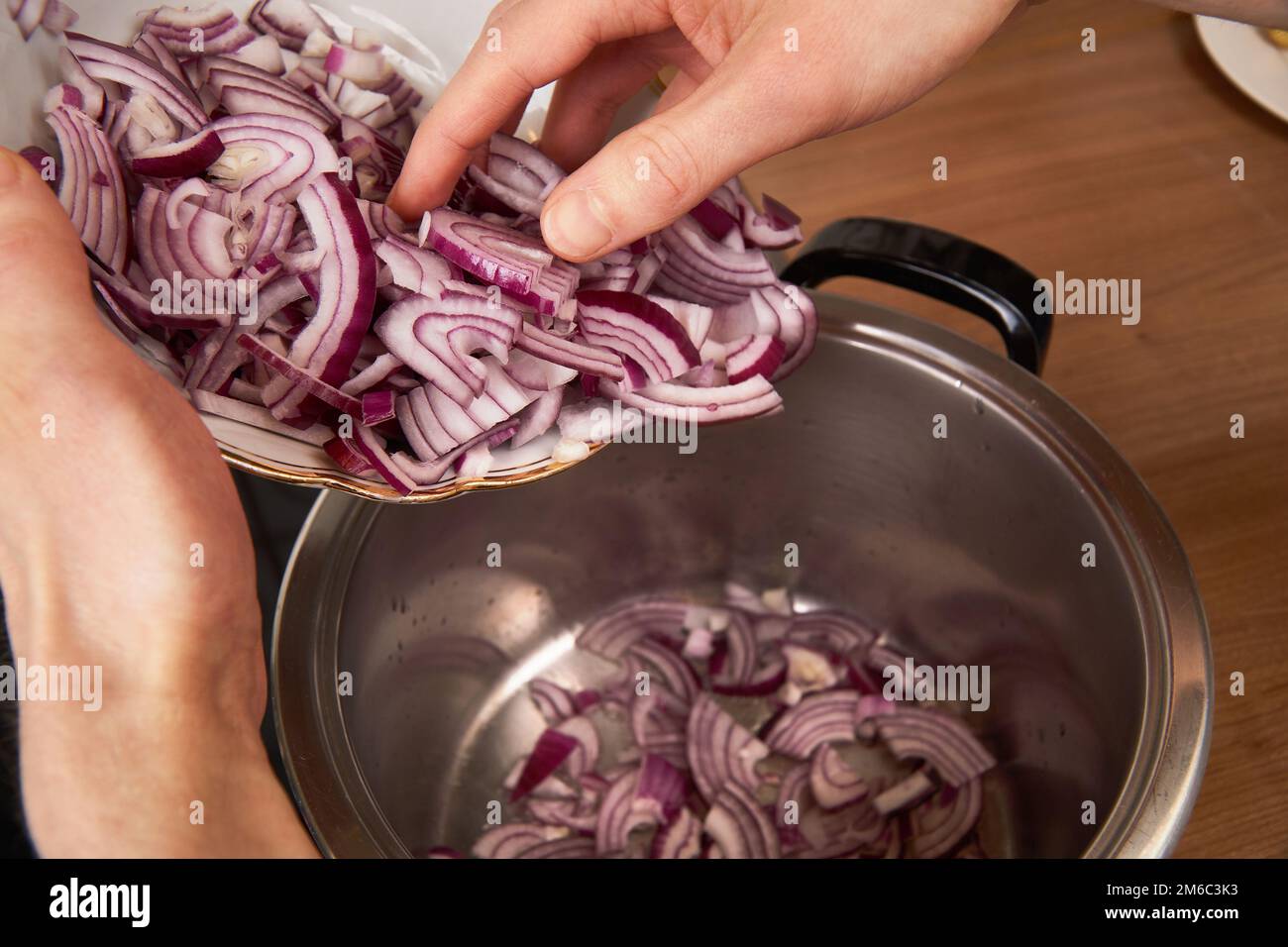 A man adds onions to pot with coconut oil to roast them gently for a meal. Stock Photo