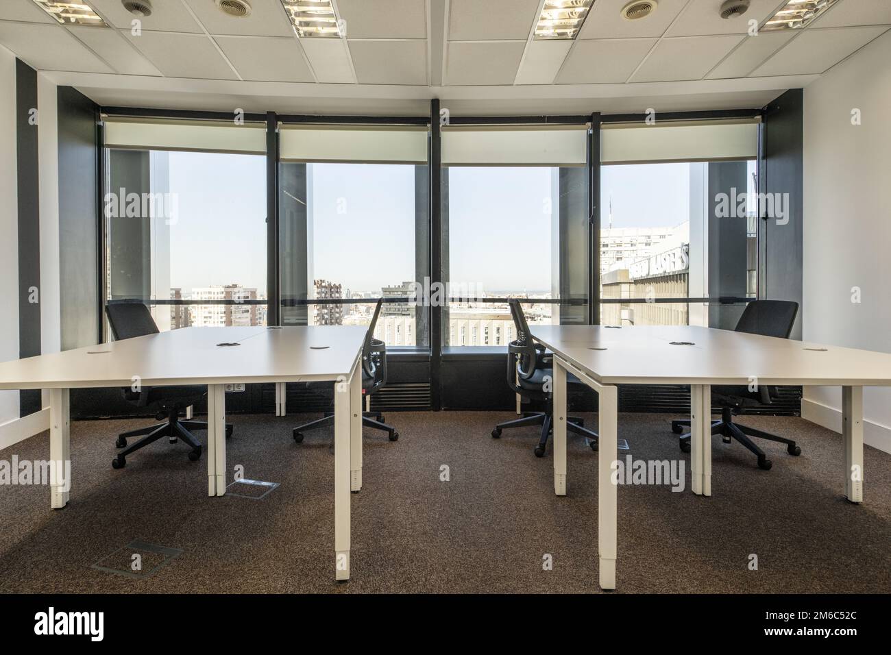 Twin white office desks with black swivel chairs and large windows