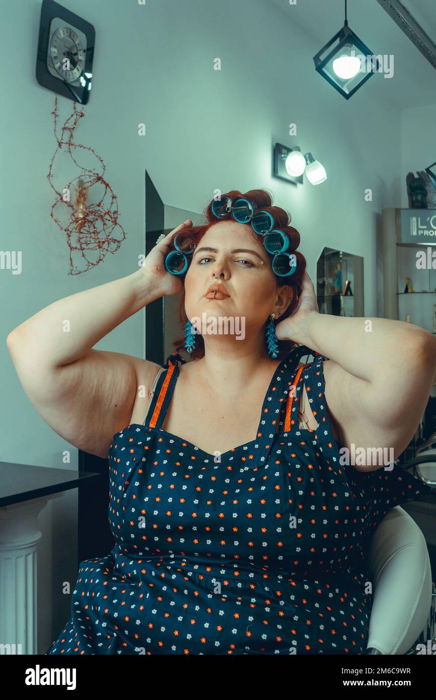 vertical portrait of argentinian caucasian young woman at the hairdresser making her hair in curlers and looking at the camera. Stock Photo