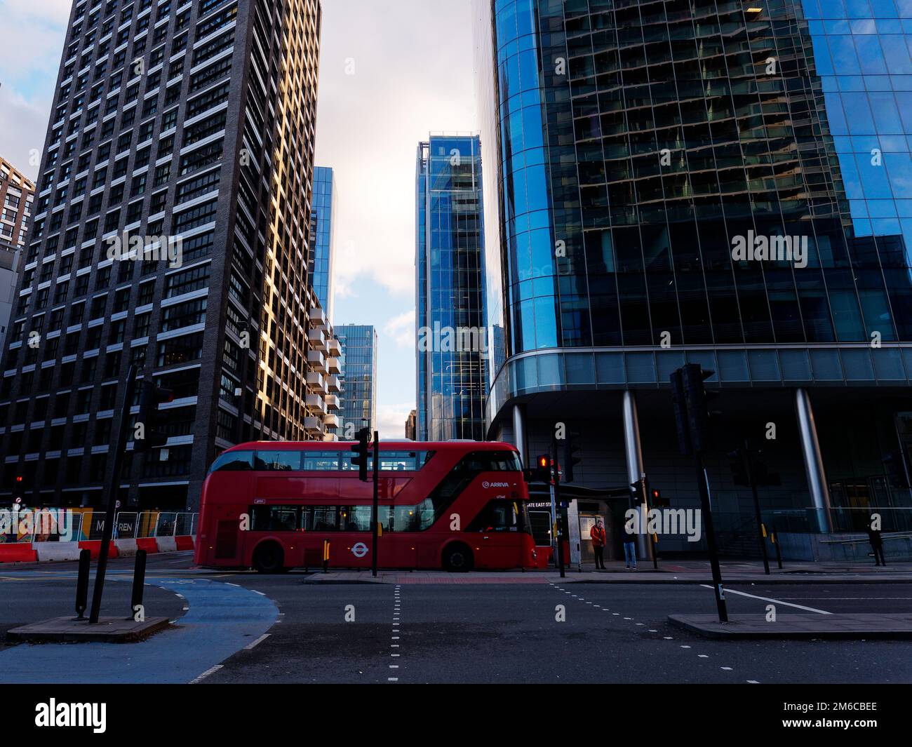 Red bus at a junction in the Aldgate East area surrounded by modern buildings approaching sunset on a winters evening. London, England. Stock Photo