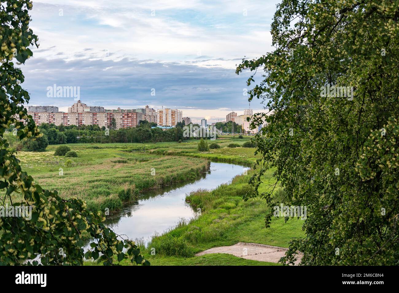 A green field with a small river can be seen the outskirts of the city Stock Photo