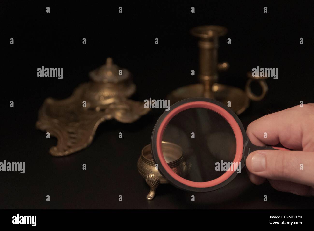 Hand with a magnifying glass while examining antique items. Expertise Stock Photo