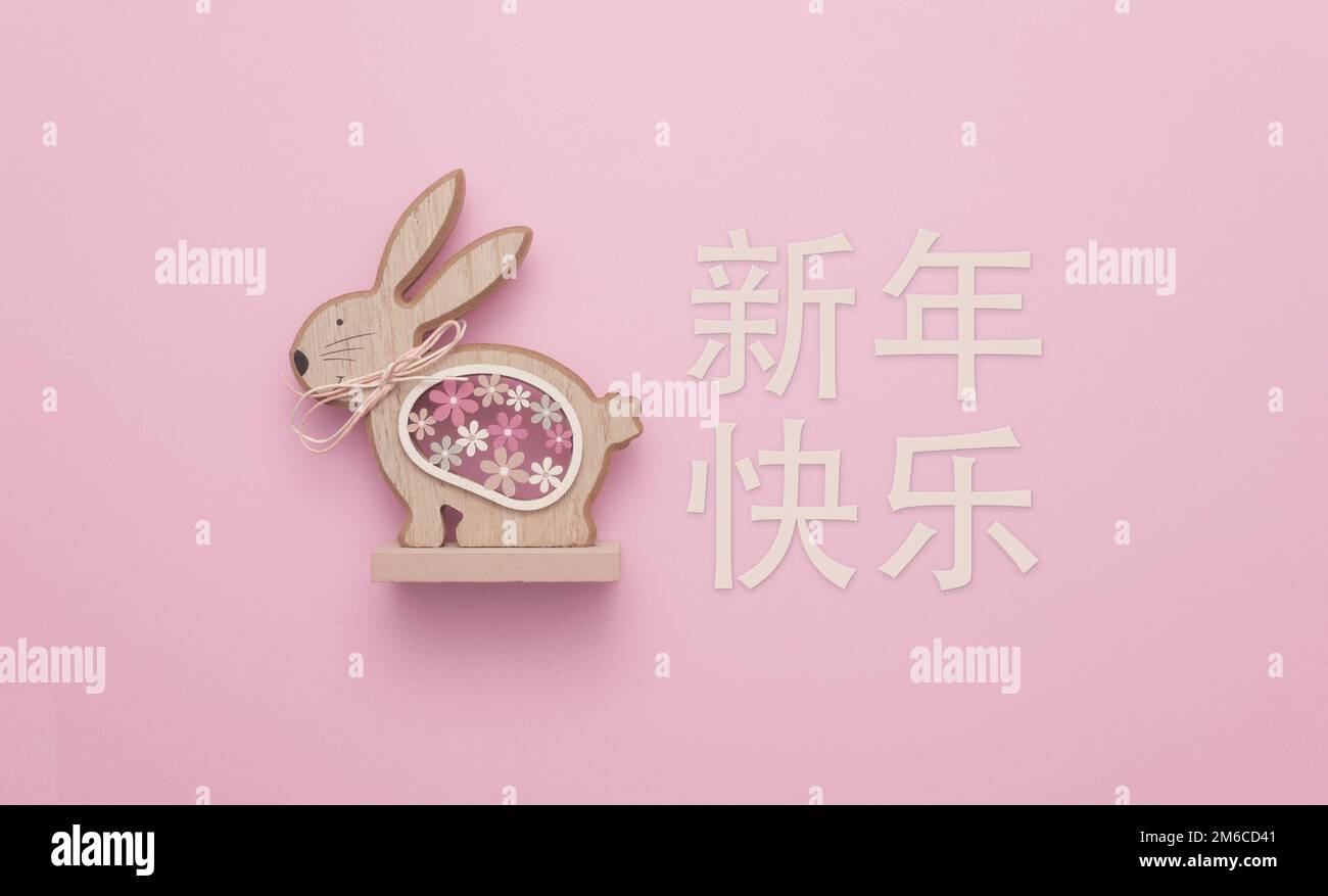 Happy Chinese New Year (新年快乐), the year of the Rabbit. A cute wooden sculpture of a rabbit against a pink background. Stock Photo