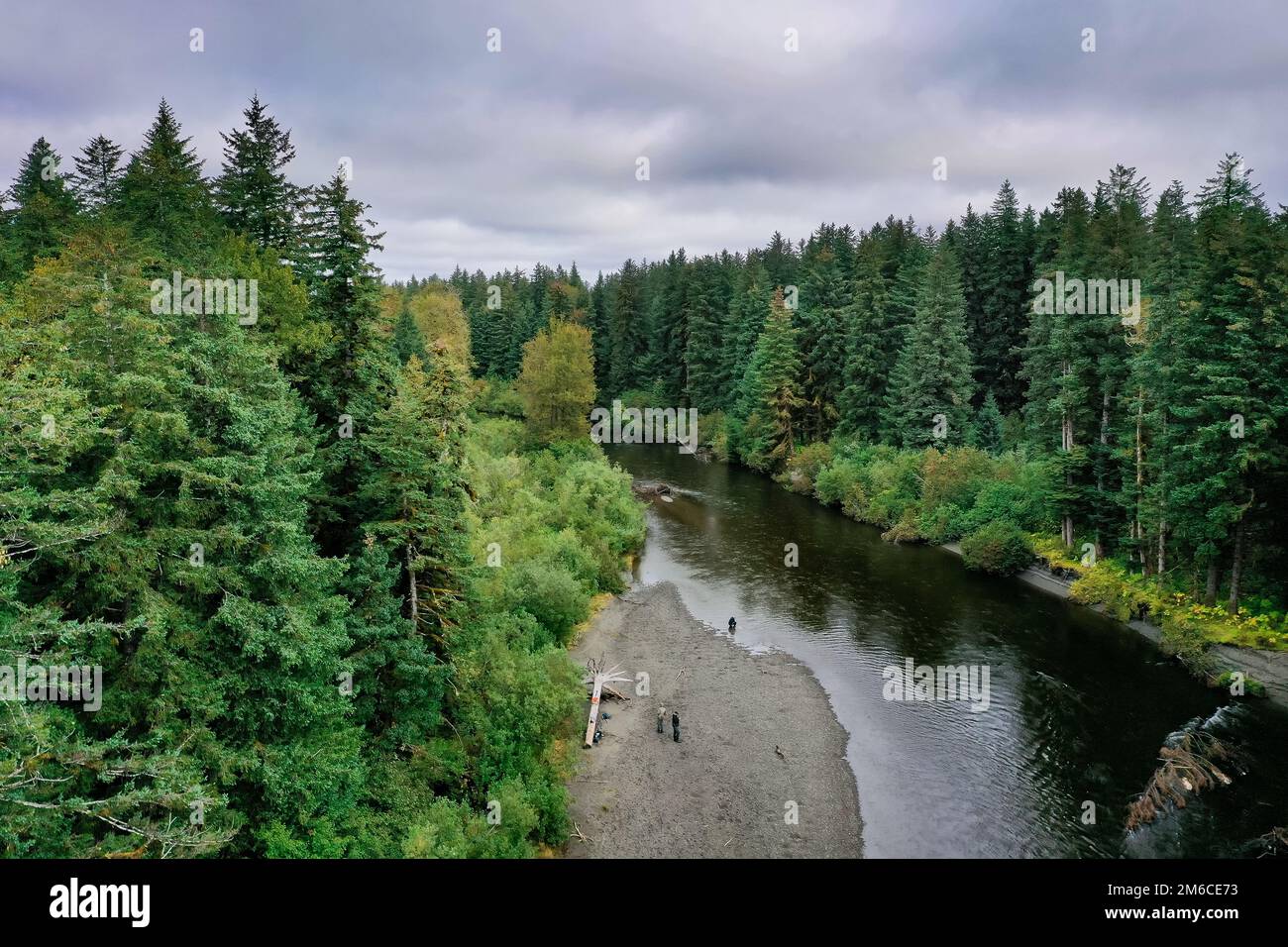 People fish along a river inside a green wilderness forest Stock Photo