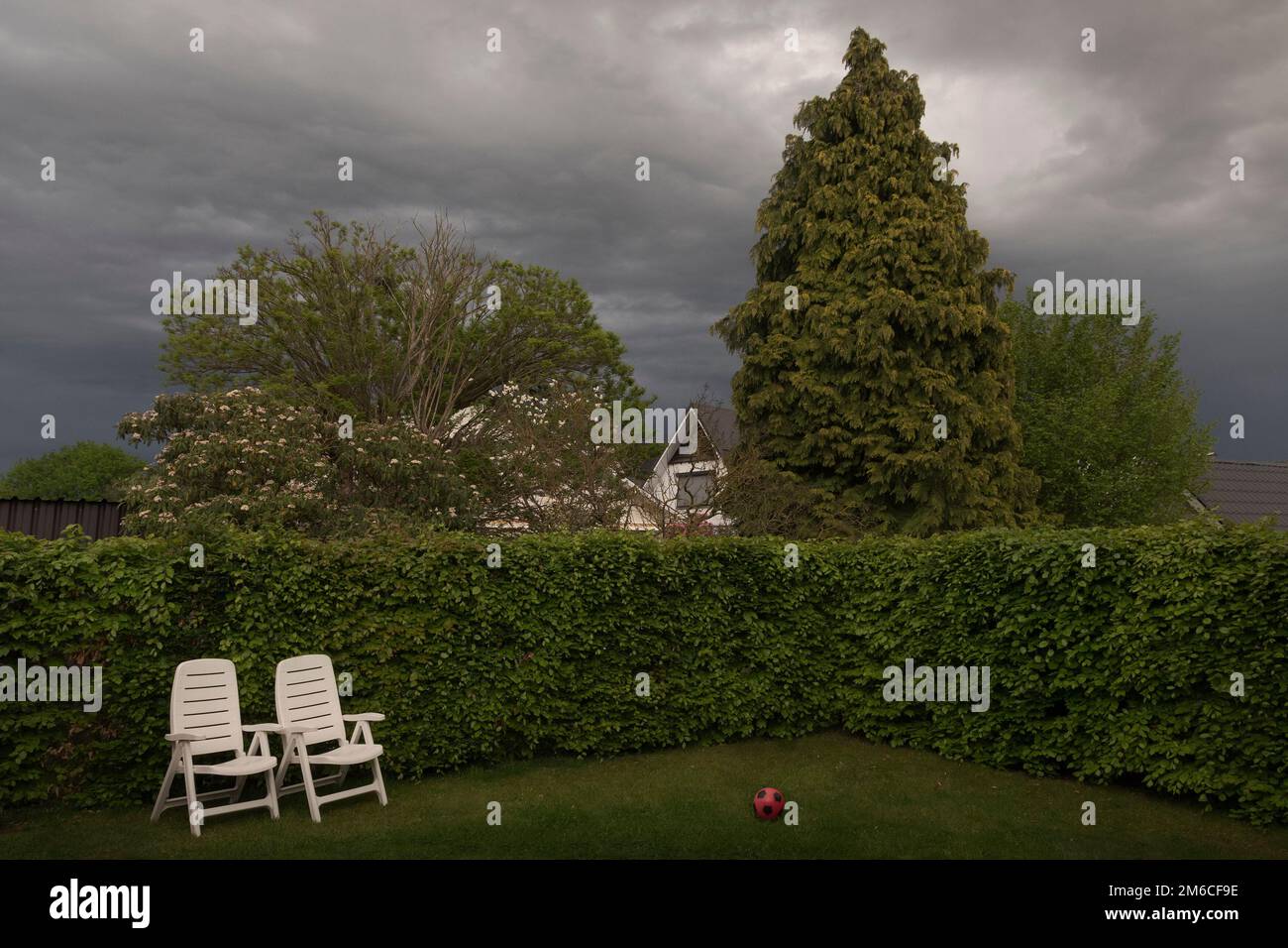 Before the rain, empty chairs and a red ball. Yard landscape in bad weather.  cloudy sky Stock Photo