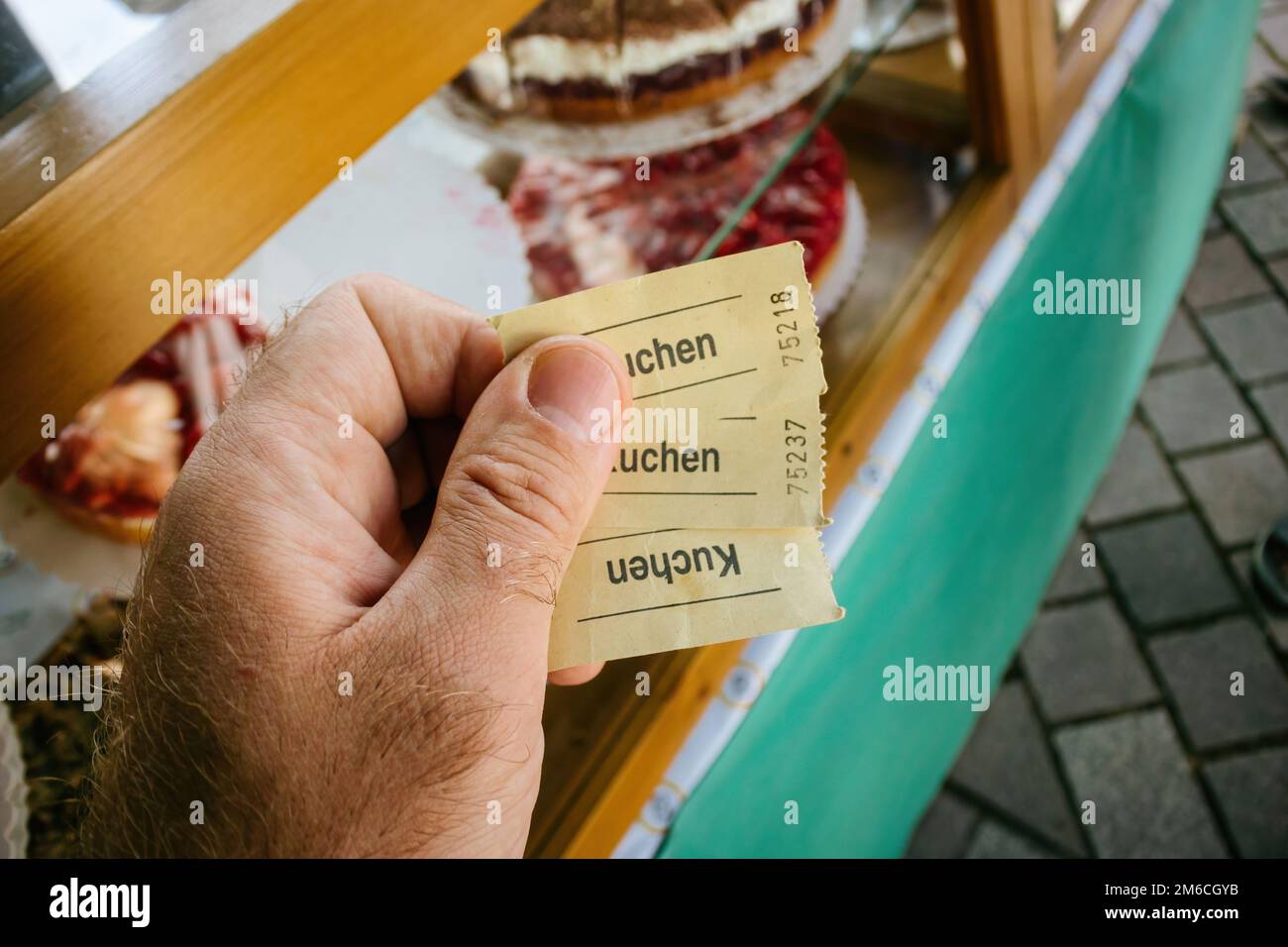 Male hand holding generic tickets with Kuchen german word printed translated as Cake - delicious pastries background Stock Photo