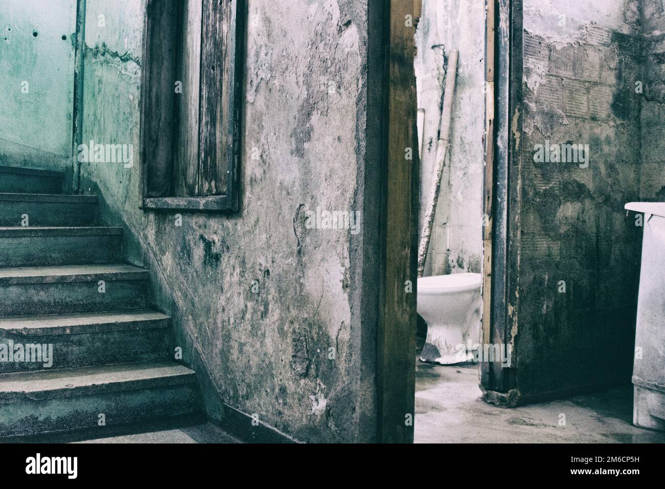 Cracked bathroom near a decayed staircase in condemned building. Stock Photo