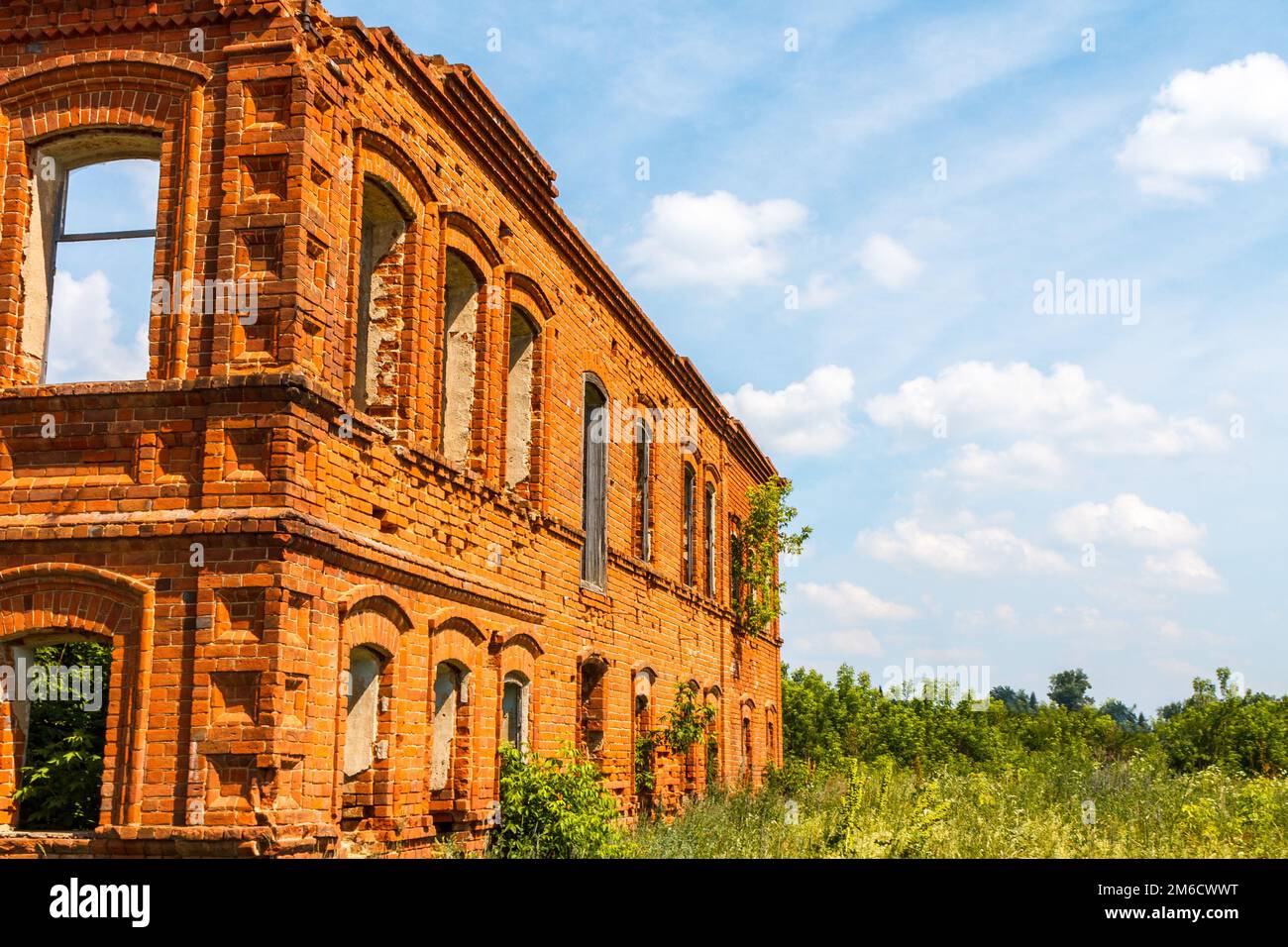 A large ruined ancient house of red brick against a blue sky with white clouds. Stock Photo