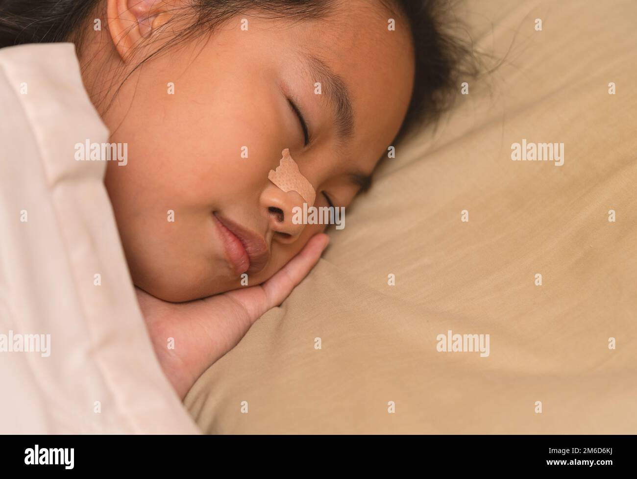 Asian child girl is sleeping well in bed, close up to the side of her face on pillow, nasal strip at her nose. Asian child girl at 8 or 9 years old. B Stock Photo