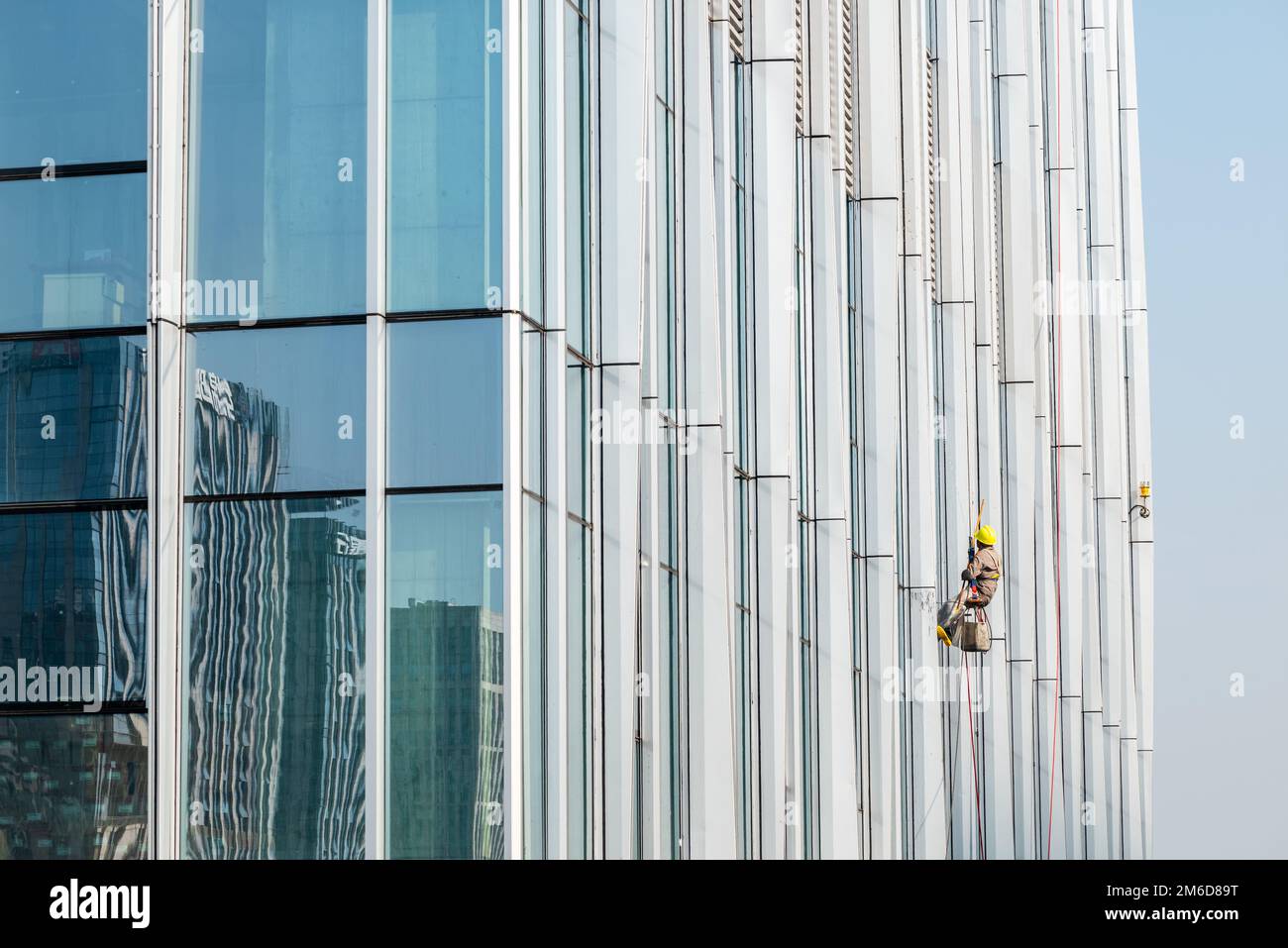 Worker cleaning skyscraper's facade windows on a sunny day Stock Photo