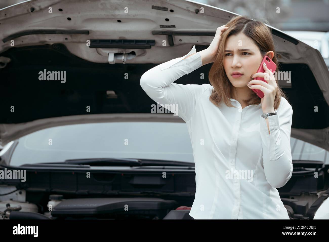 Young woman calling emergency help near broken car on road. Stock Photo