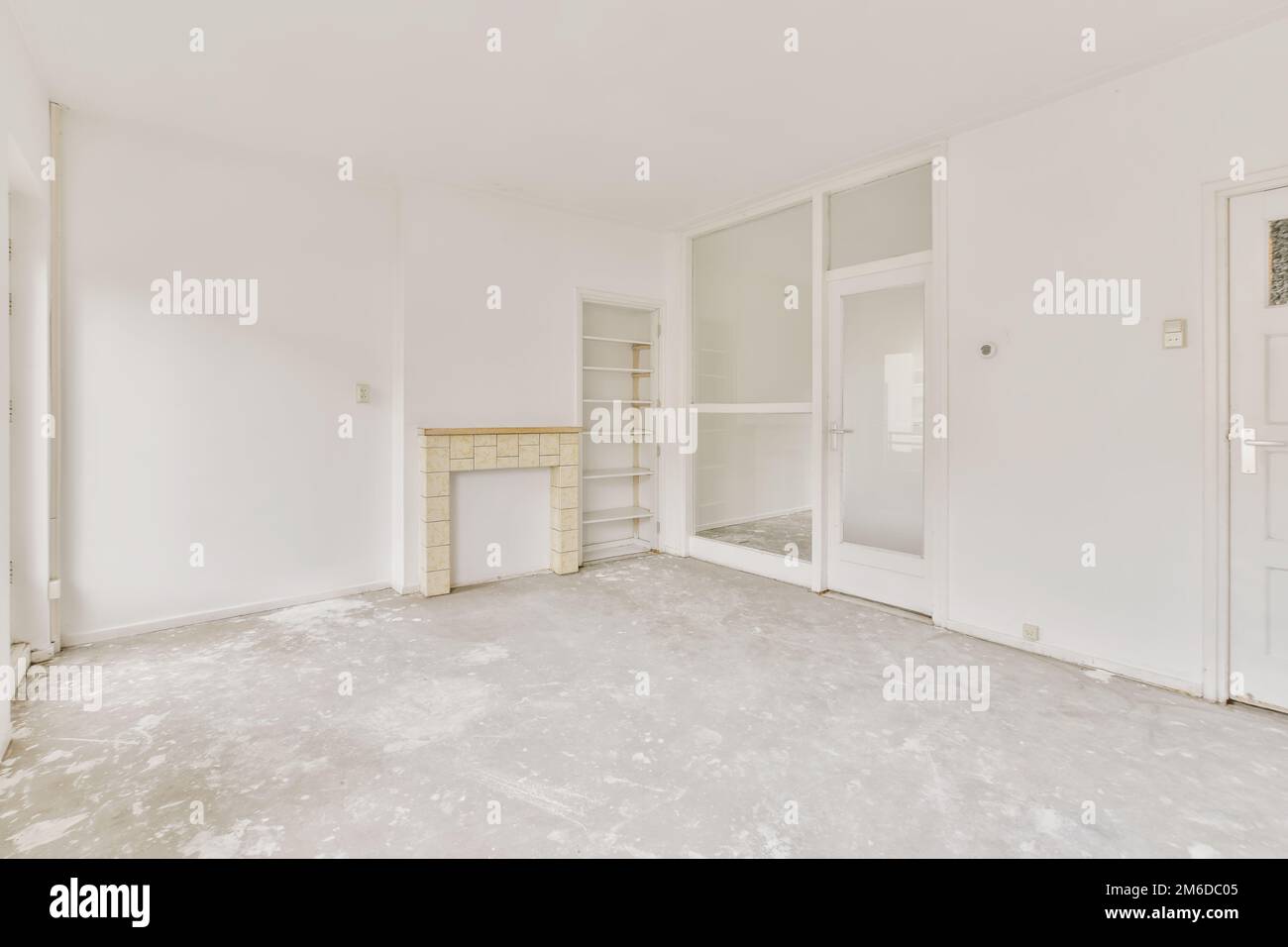 an empty living room with white walls and floor to the right, there is a large mirror on the wall Stock Photo