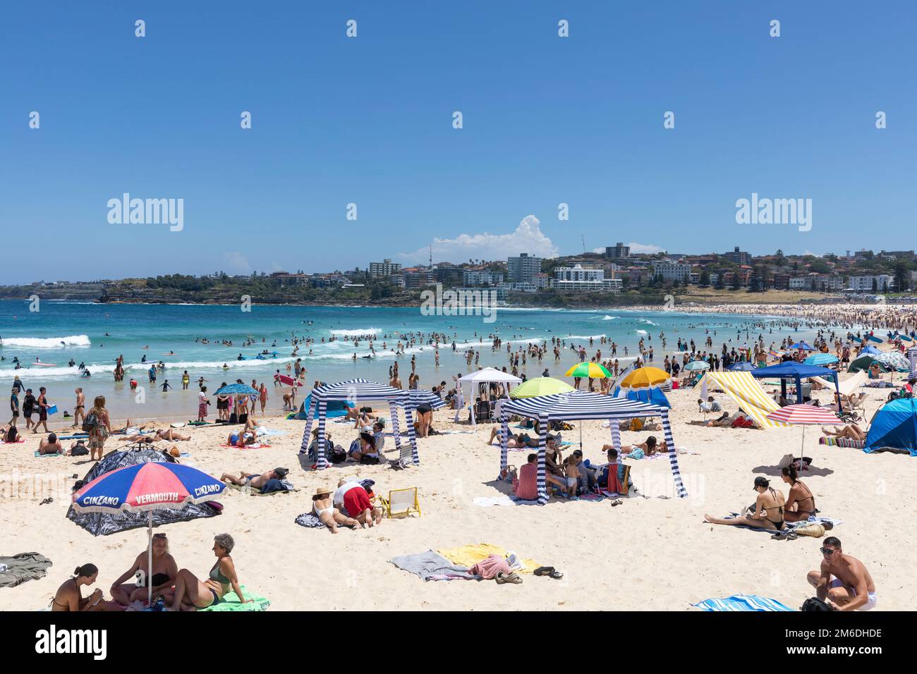Crowded Bondi Beach summer 2023, people sunbathe and seek shade under