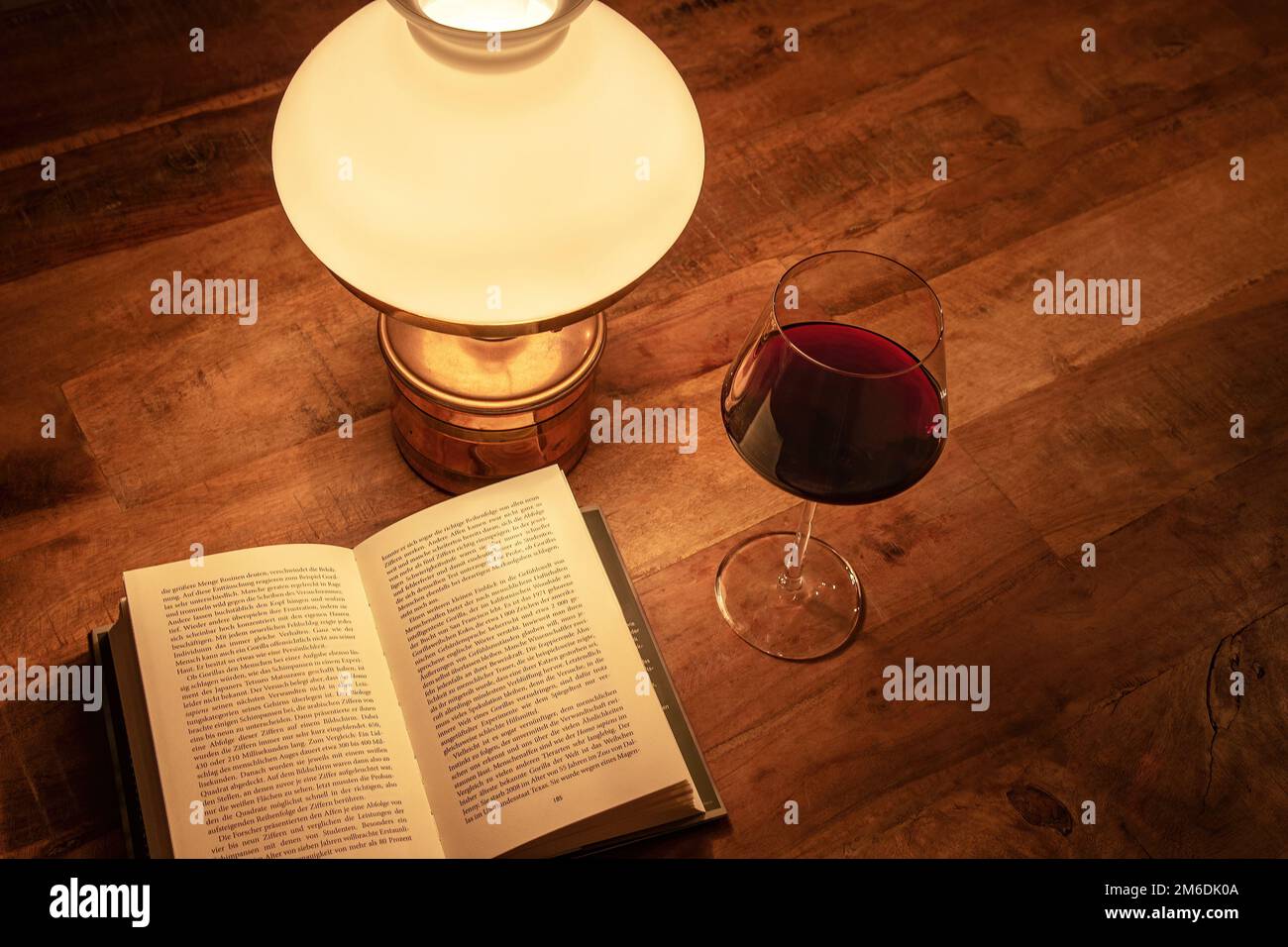 Old table lamp with book and glass of red wine on old wooden table Stock Photo