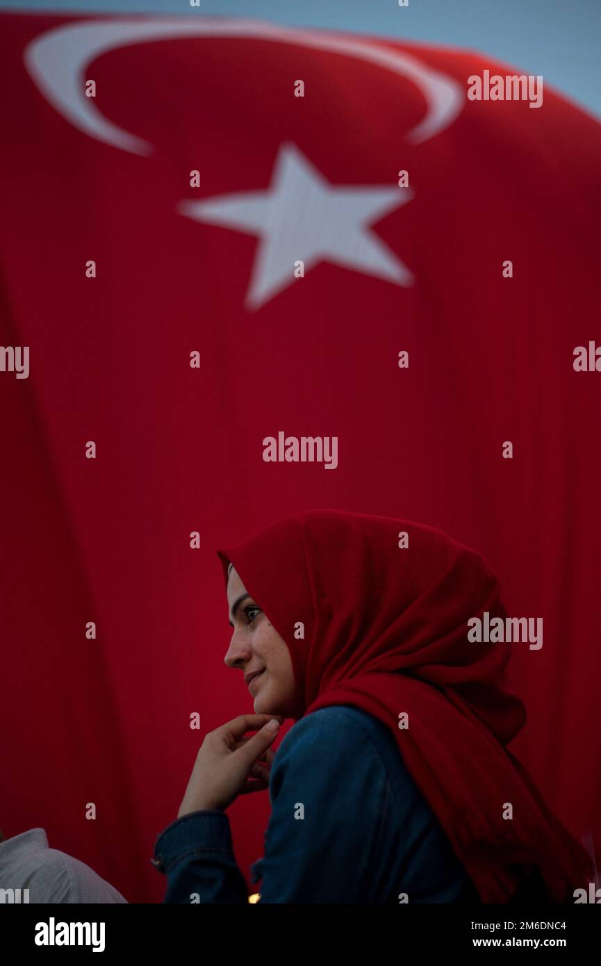 Turkish Muslim Woman with red headscarf with Turkish flag behind attending a pro government rally in Stock Photo