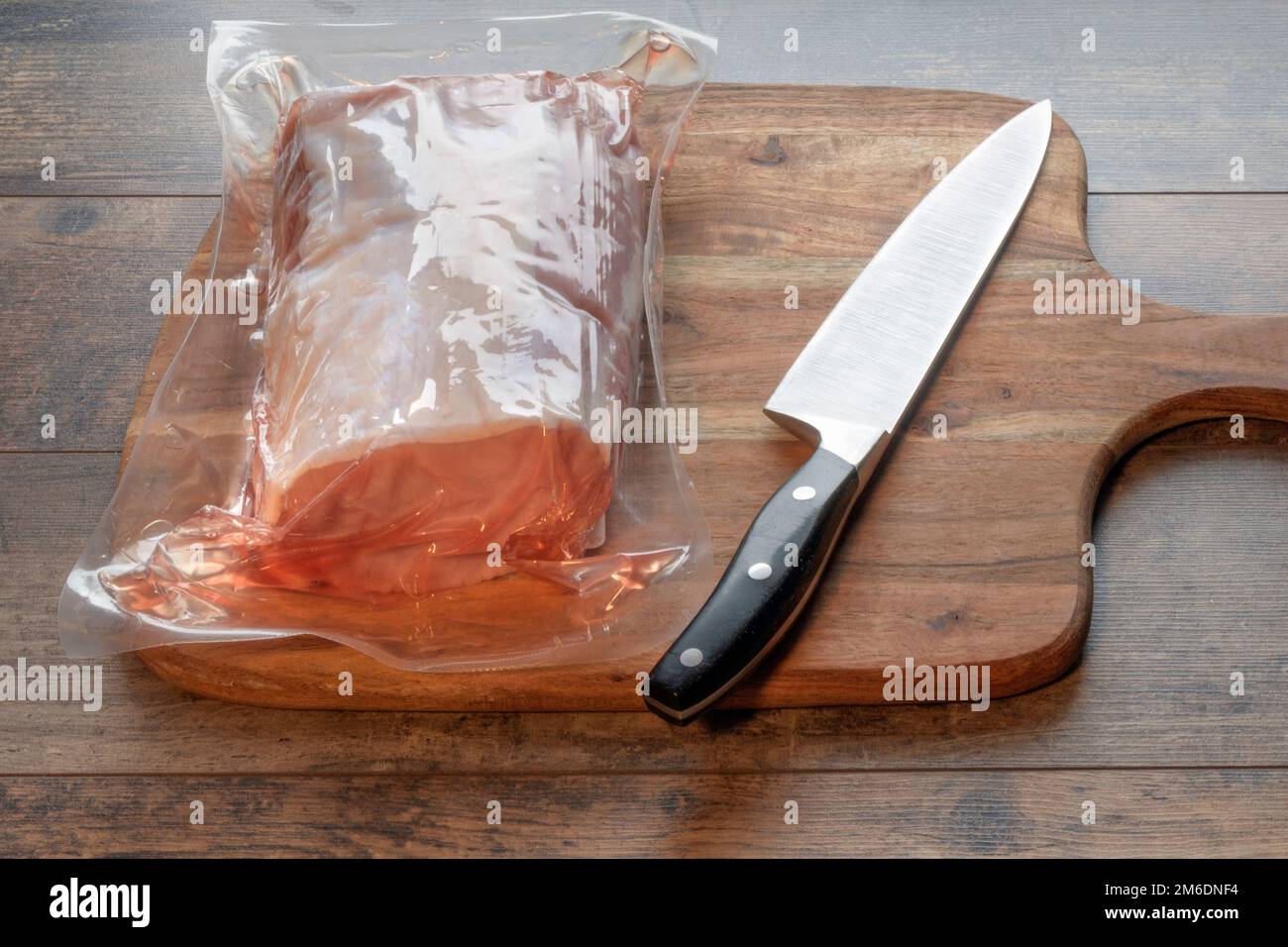A vacuum-packed pork tenderloin on a cutting board in the kitchen Stock Photo