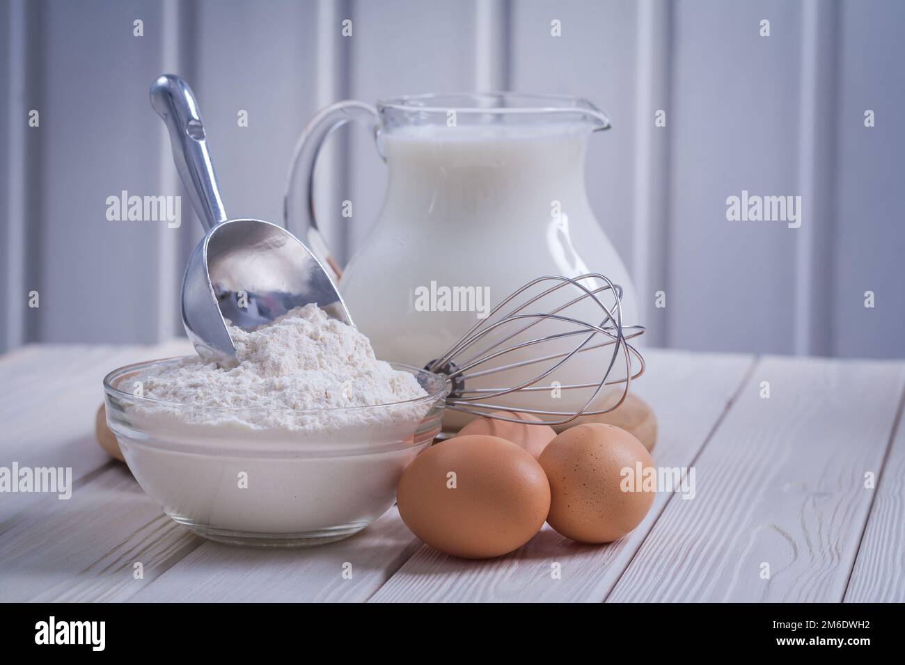 composition of kitchen objects eggs corolla bowl with flour pitcher milk on white painted old wooden board food and drink concept Stock Photo