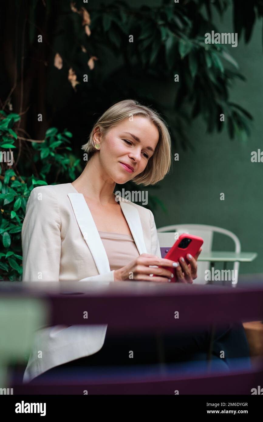 Woman using a mobile phone while sitting outdoors. Stock Photo