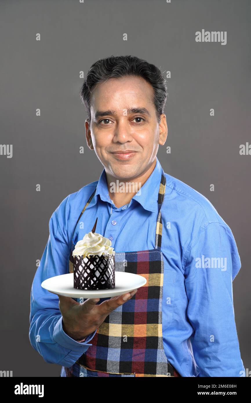 Indian Male Chef with a Sweet Dish Cake on grey Background Stock Photo