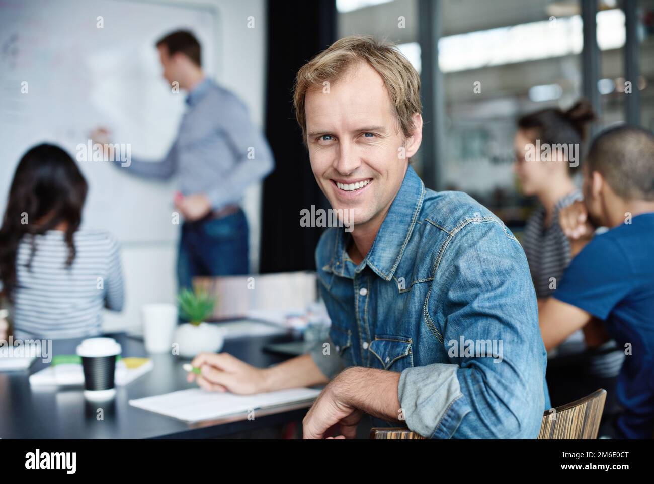 We make ideas a reality. Portrait of an office worker with his colleagues sitting in the background. Stock Photo