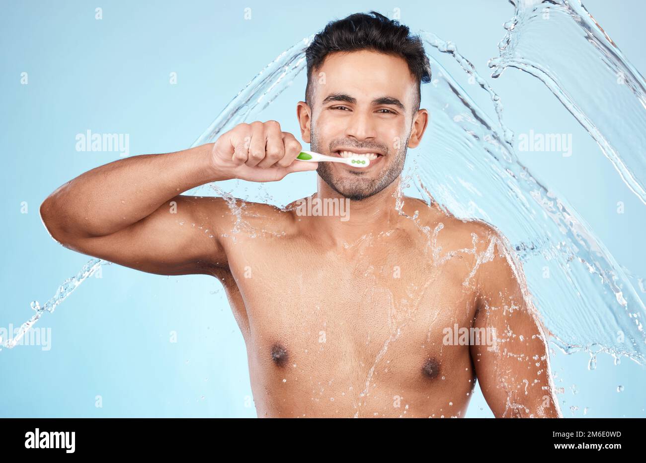 Face, water splash and man with toothbrush for cleaning in studio on blue background. Dental veneers, hygiene and portrait of happy male model Stock Photo
