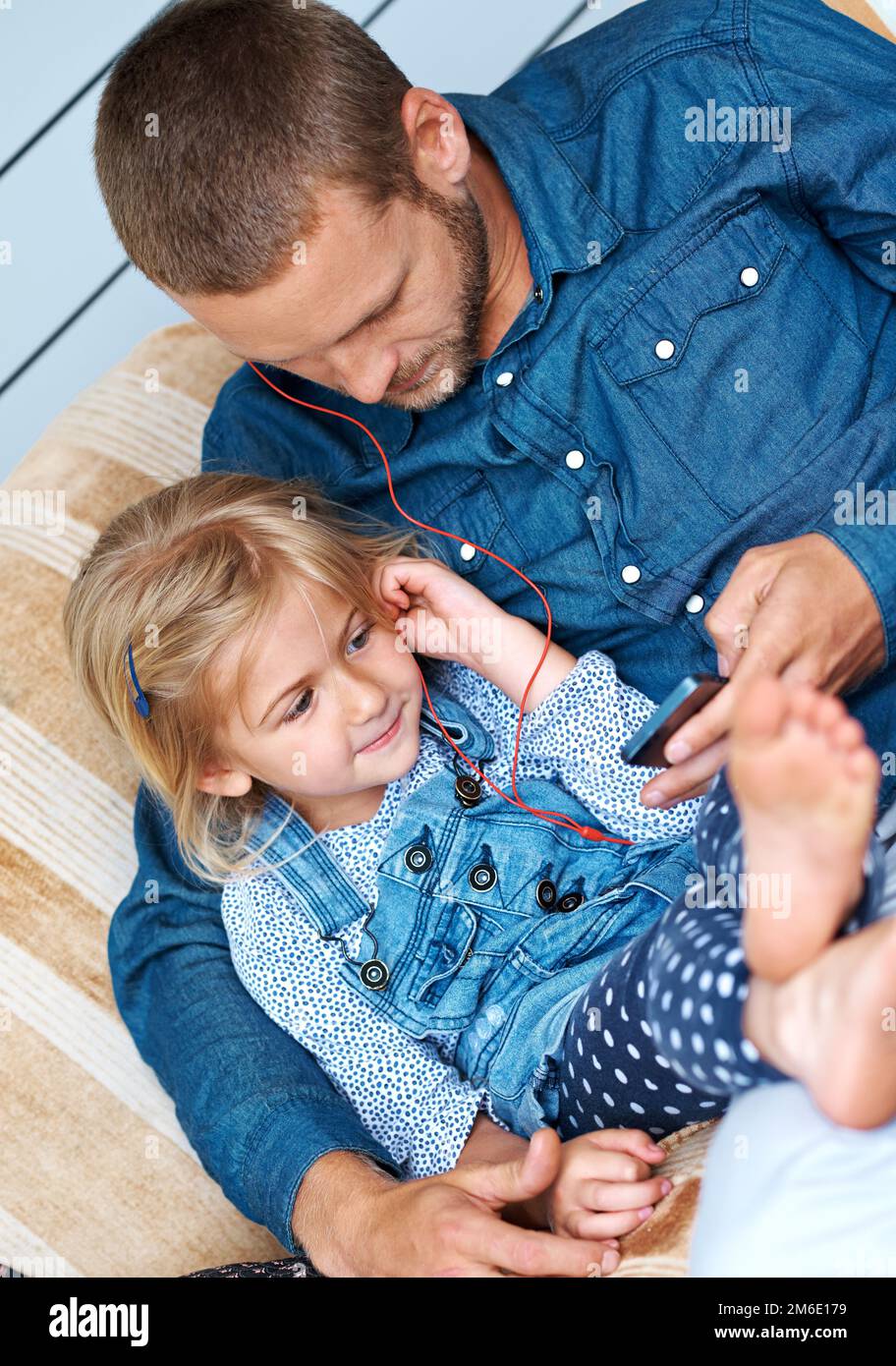 Choosing their next track. an adorable little girl sitting on the sofa sharing headphones with her father. Stock Photo