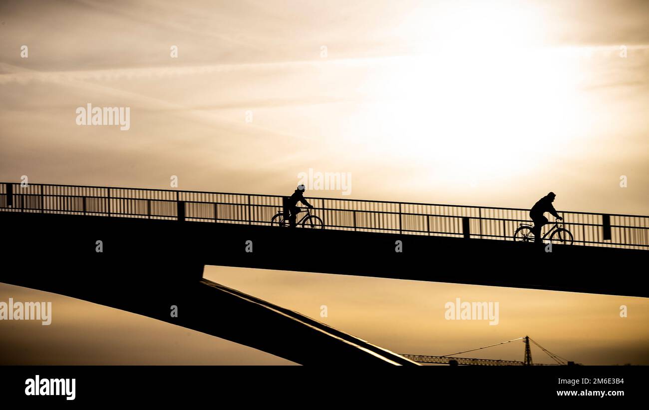 A bike-rider drive down the bridge in the late backlight sun near ...