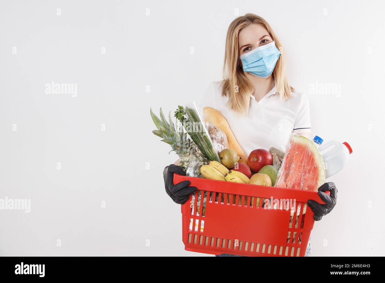 Young woman shopping during a pandemic. Girl in medical mask with basket of products. Shopping times Stock Photo