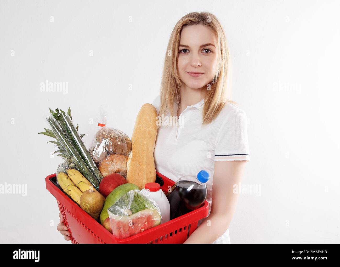 Young woman with goods in basket. Girl holding a basket of groceries. Vegetables, fruits, cookies, milk in the grocery basket. Stock Photo