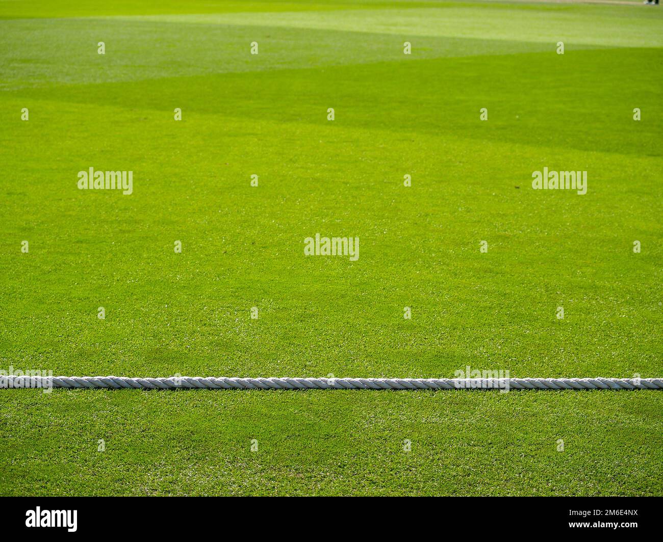White rope divides green lawn as boundary rope on cricket pitch. Stock Photo