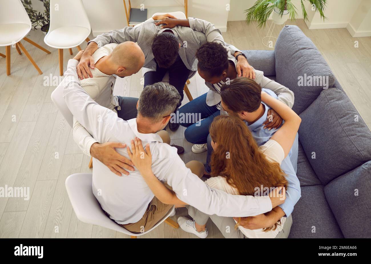Support group consisting of different people sits in circle and hugs all together at meeting. Stock Photo
