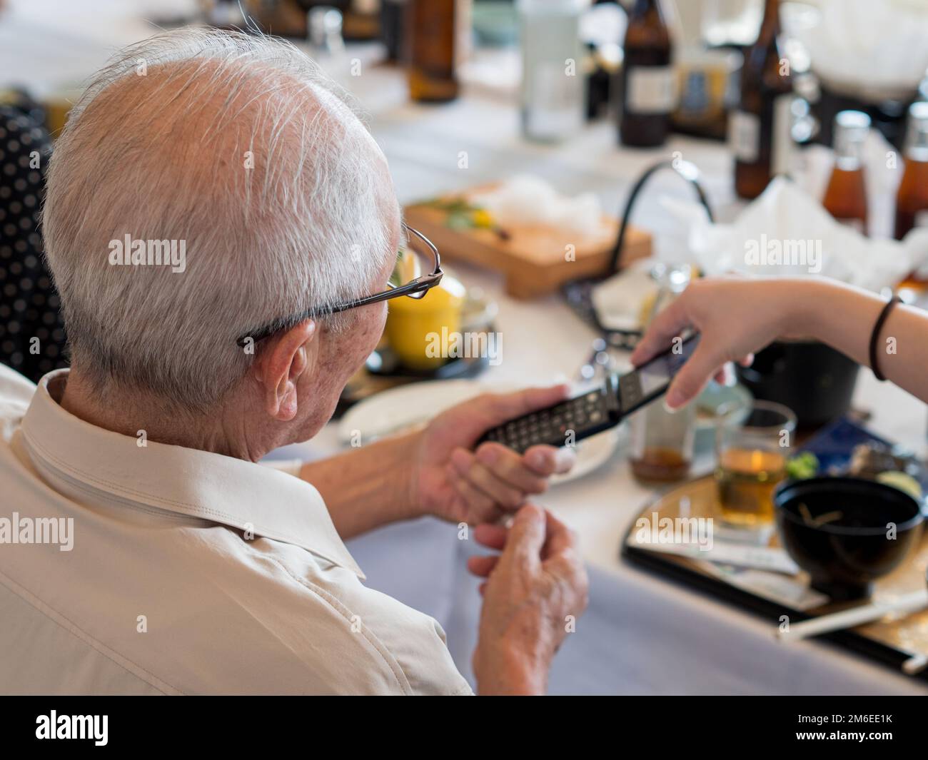 An elderly Asian man struggling to use an old fashioned flip phone Stock Photo