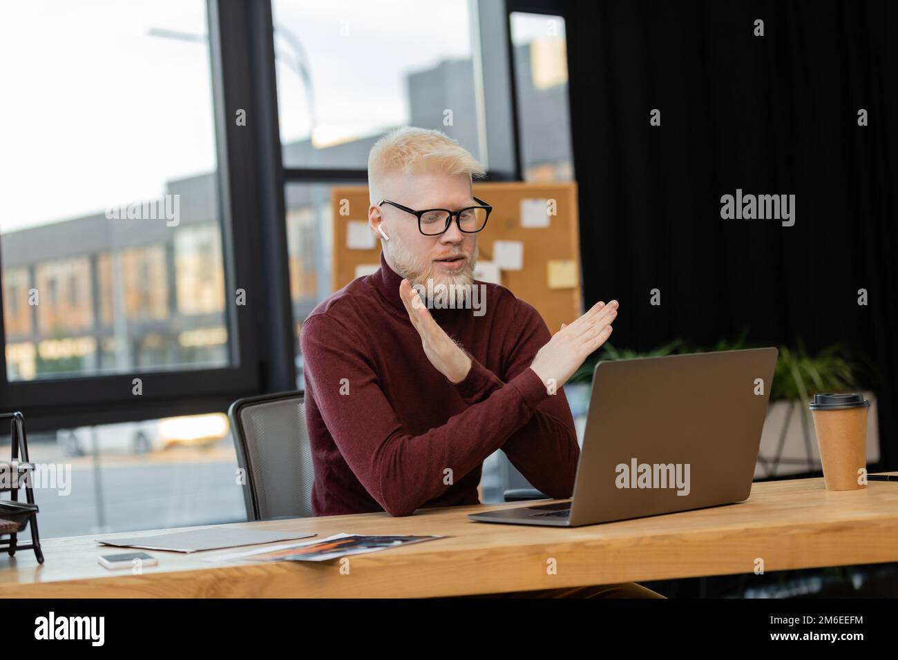 bearded albino businessman in earphones showing refuse gesture during video call on laptop while working in office,stock image Stock Photo