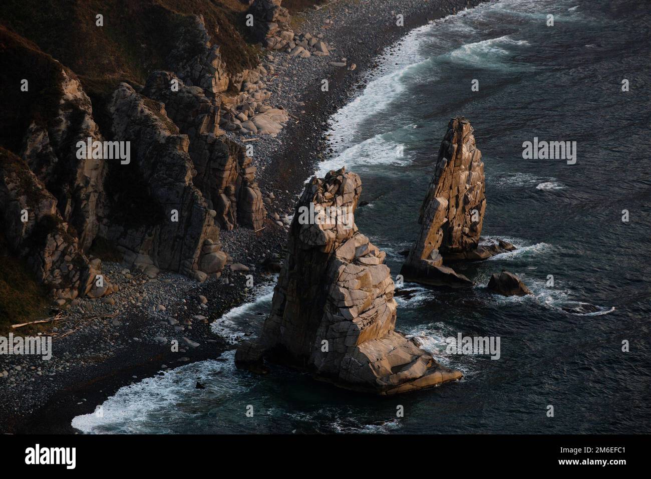 A huge stone in the form of an arch stands in the middle of the sea against the background of sheer cliffs. The territory of the Stock Photo