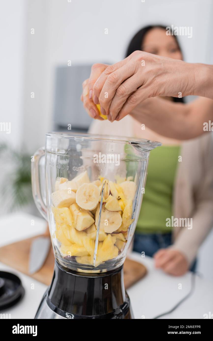 Mature woman squeezing lemon while preparing fruit smoothie with friend in kitchen,stock image Stock Photo