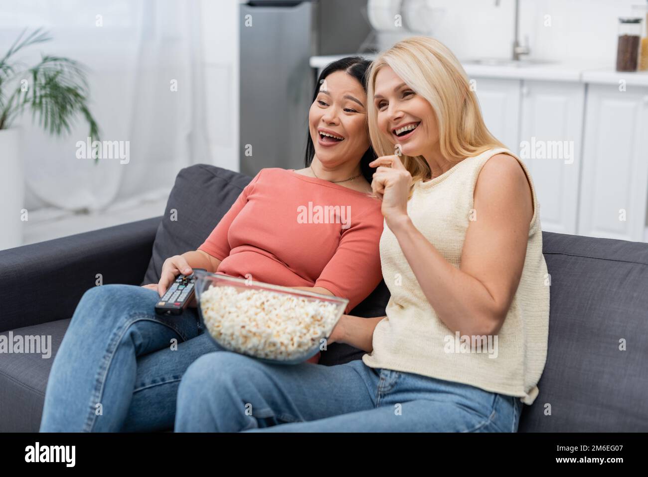 Cheerful multiethnic women with remote controller and popcorn watching