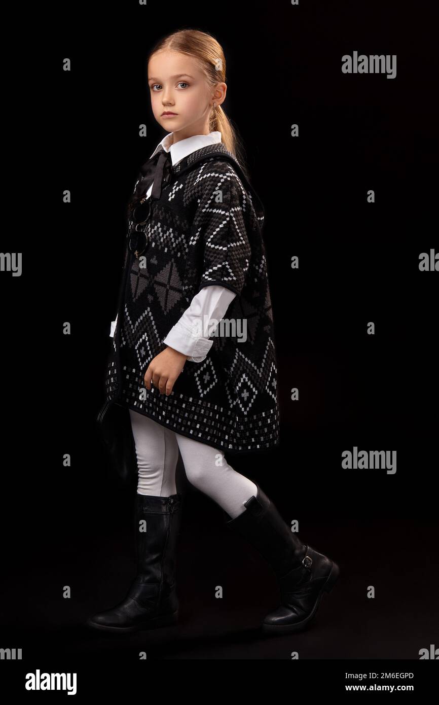 Little girl in a dark poncho, black boots and a clutch in her hand Stock Photo