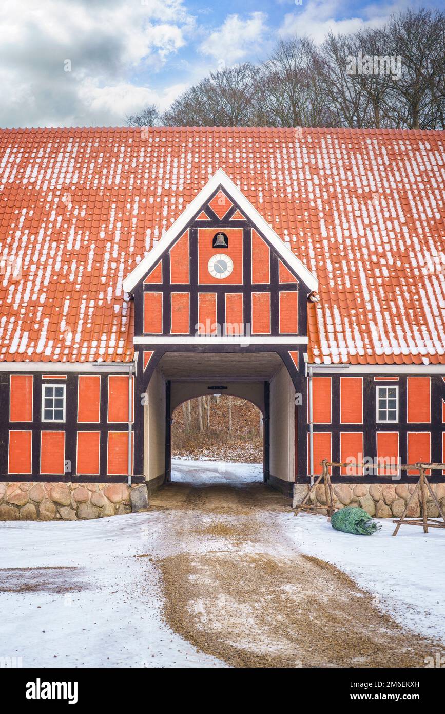 Red farm house with an open gate in the winter with a clock and a bell Stock Photo