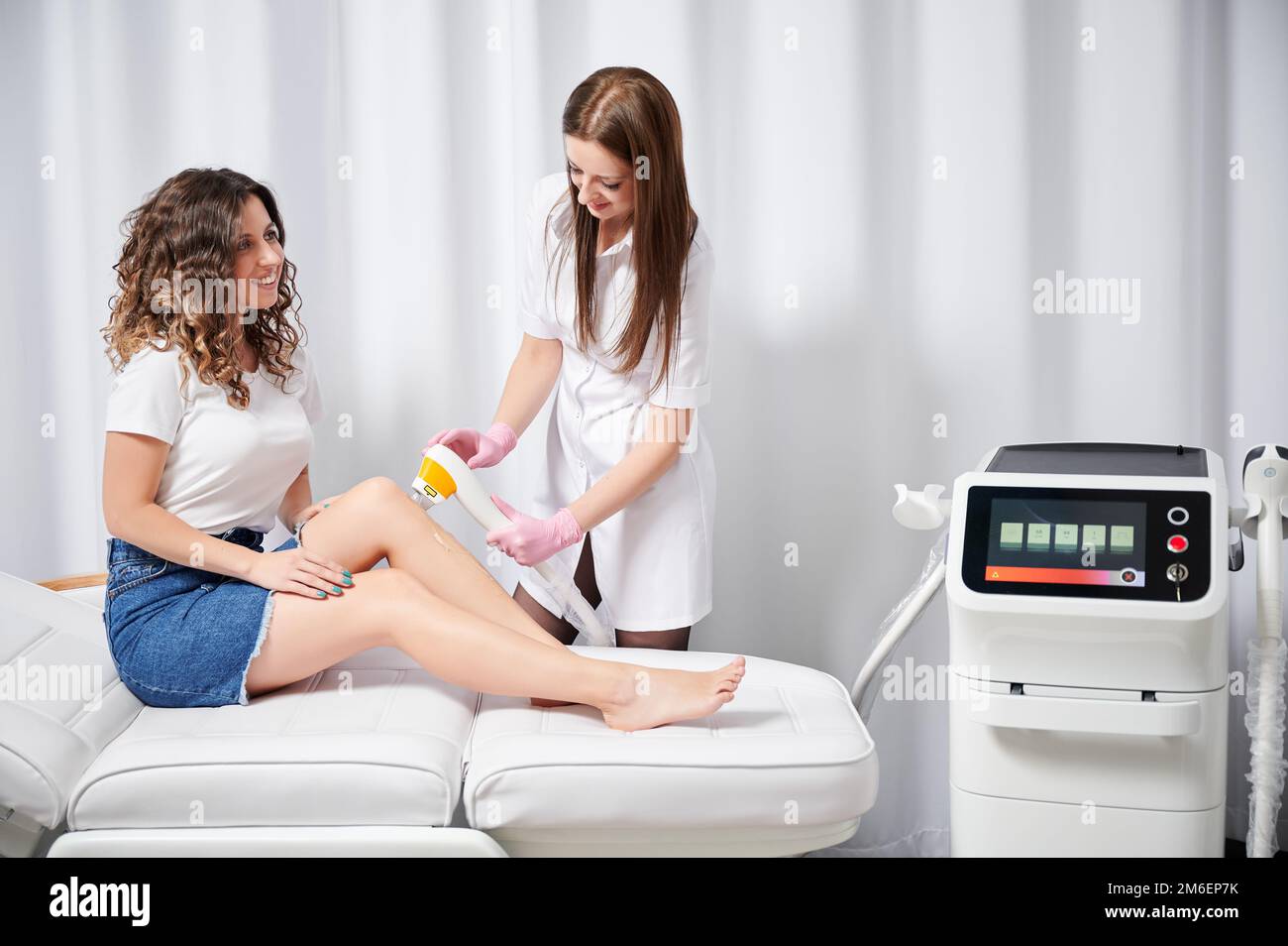 Young cosmetologist performing procedure of laser removal of unwanted