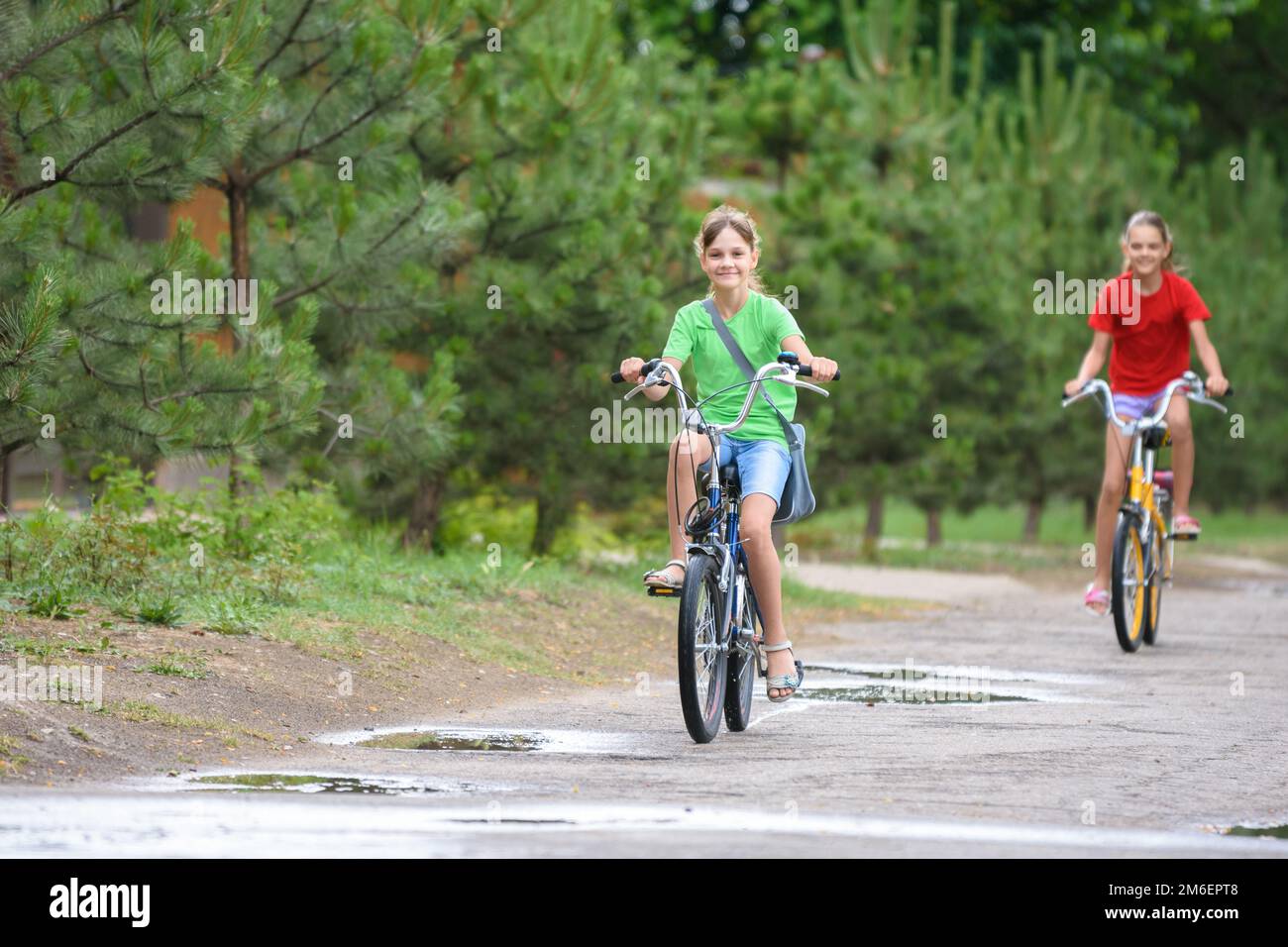 Two girls ride a bike on a rainy warm day Stock Photo