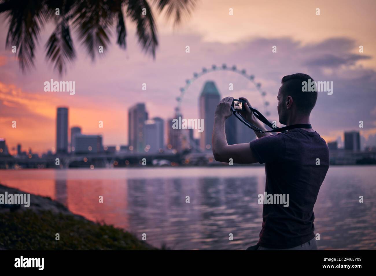 Man photographing Singapore urban skyline at beautiful sunset. Tourist