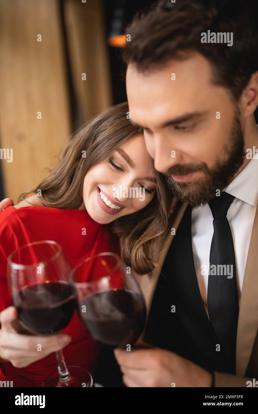 happy woman and bearded man clinking glasses with red wine during ...