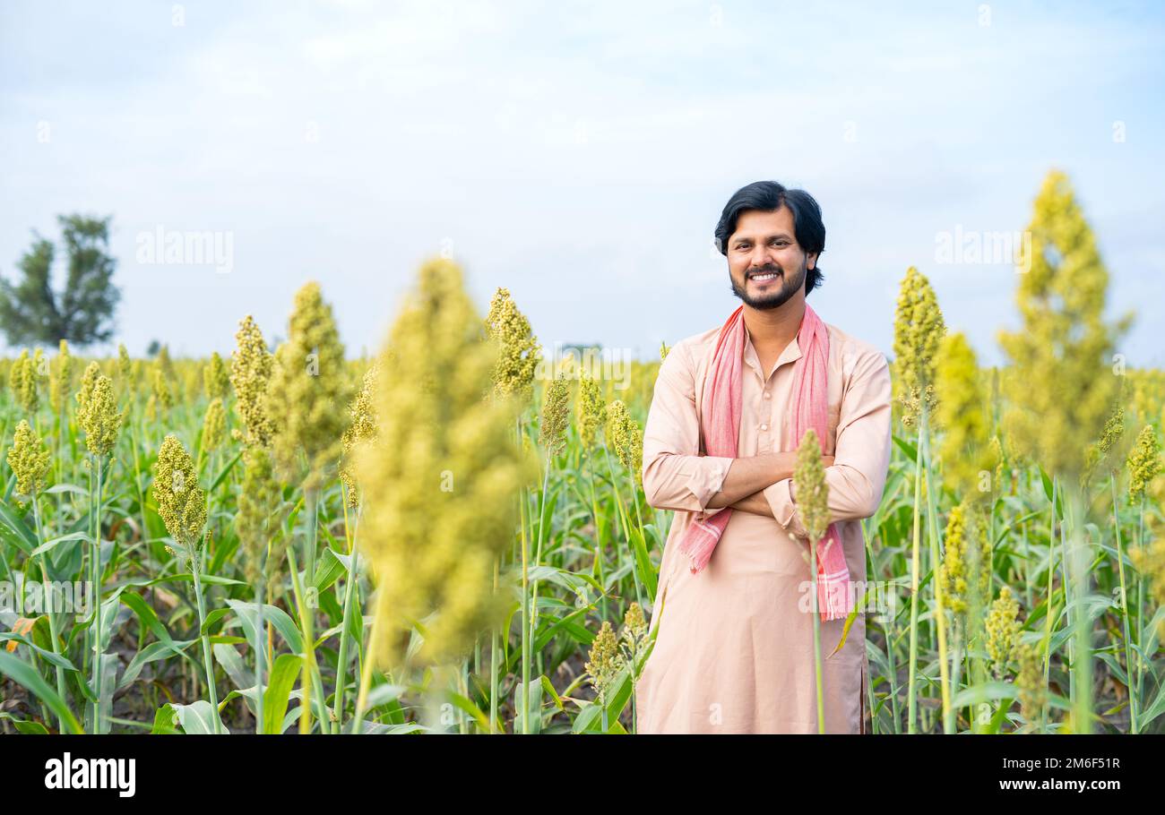 Confident young indian farmer standing with crossed arms by looking camera at farmland - concept of successful farming, and agricultural Stock Photo