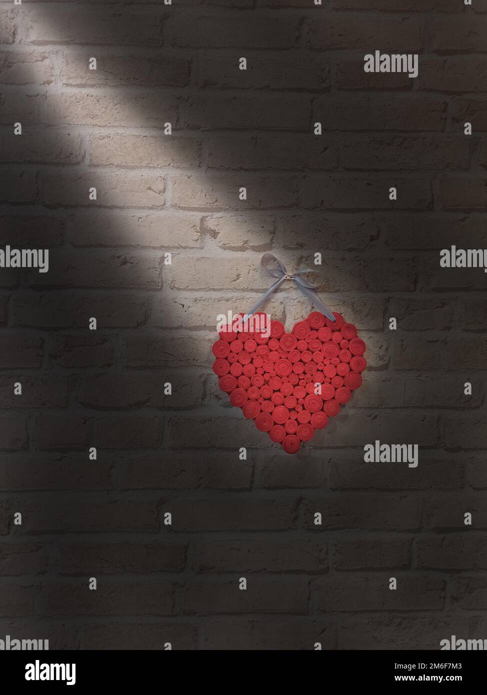 Ray of light falling on heart hanging on brick wall. Light illuminating heart in darkness. Love in b Stock Photo