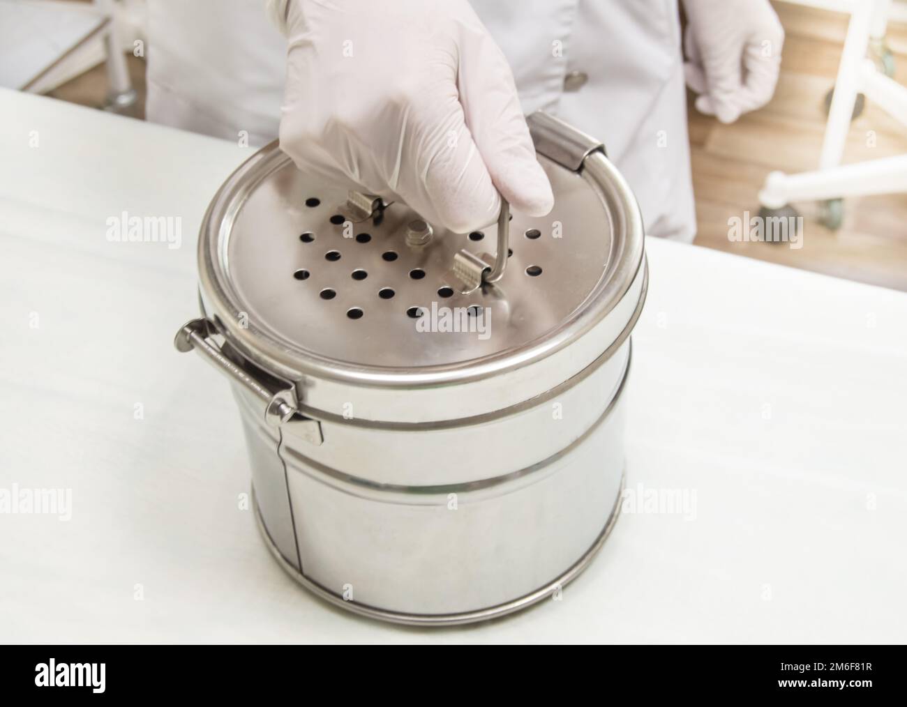 Round stainless steel sterilizer in the hands of a nurse in rubber