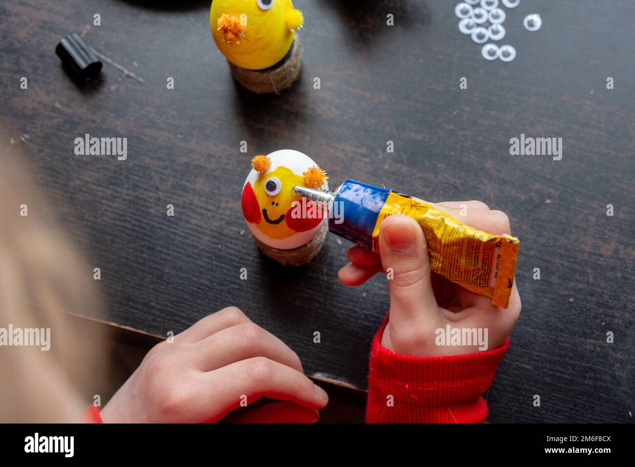 A girl decorates an egg for easter and glues funny eyes to it Stock Photo